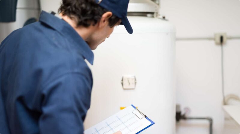 a plumber holding a clipboard with papers while inspecting a residential water heater