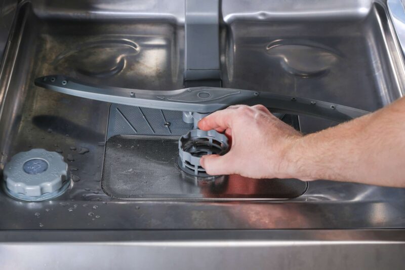 a hand reaching out to inspect a dishwasher that won't drain