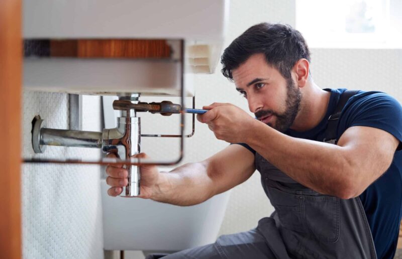 a plumber sitting down in order to provide a repair for a bathroom plumbing problem