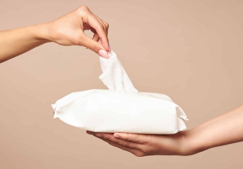 a hand reaching to grab a flushable wipe from a pack that's being held by another person