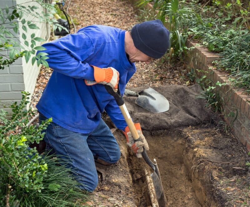 a man using a shovel to uncover a pipe for sewer line repair services