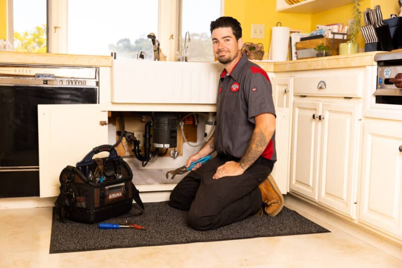 a Gotelli plumber kneeling down to provide plumbing services for a clogged sink