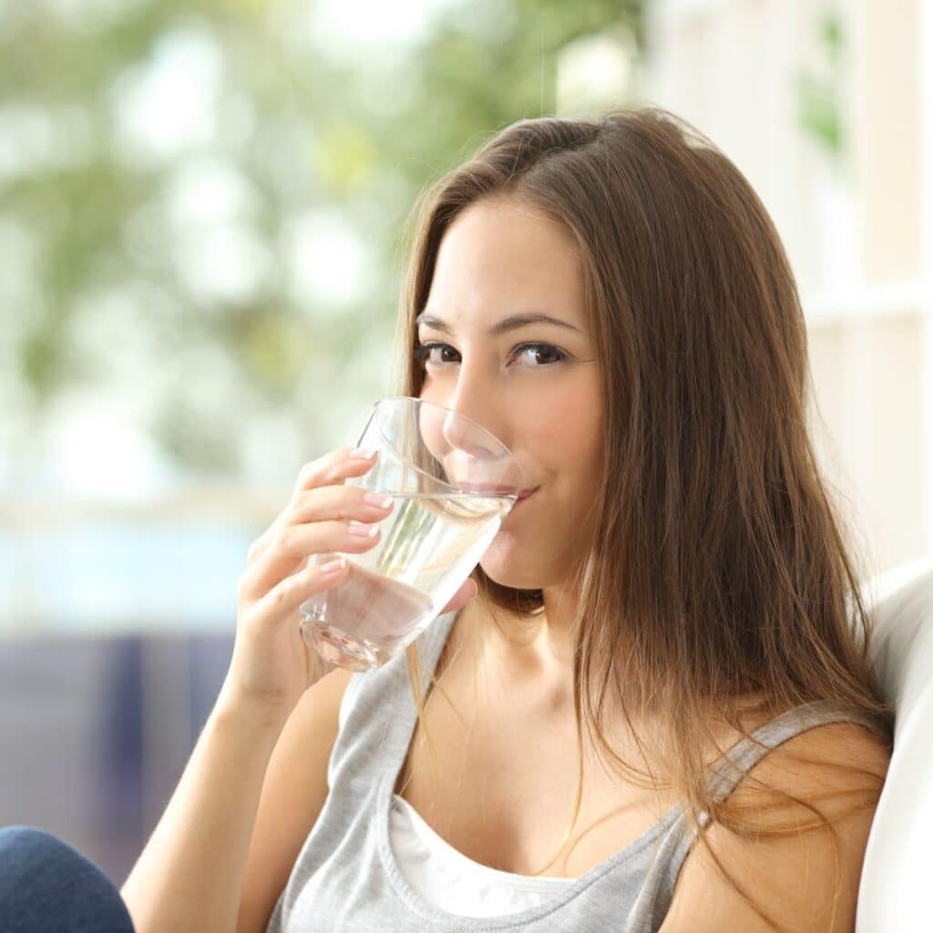 woman sitting on a couch while drinking a glass of filtered water