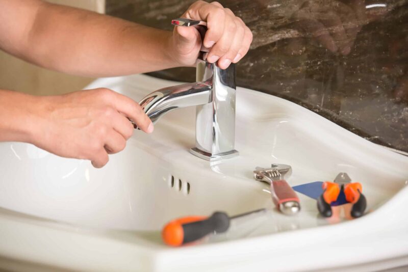 plumber providing bathroom sink plumbing services by repairing a sink faucet