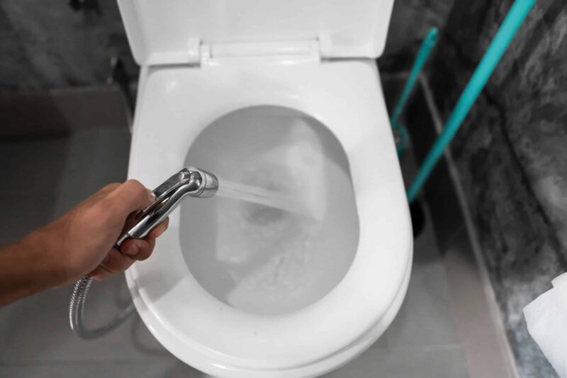 a hand spraying water from a hose into the bowl of a bidet toilet