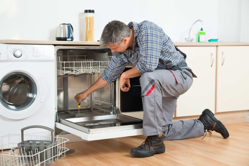 a plumber using a screwdriver to provide dishwasher repairs