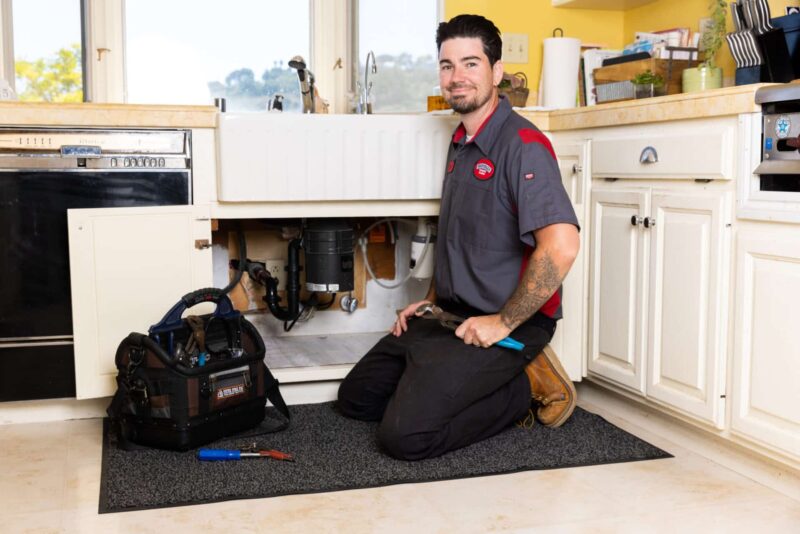 a Gotelli plumber kneeling in front of a sink to inspect it for leaks