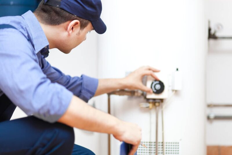 a plumber kneeling down while adjusting settings on a water heating system