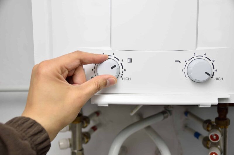 a hand adjusting a dial on a tankless water heater