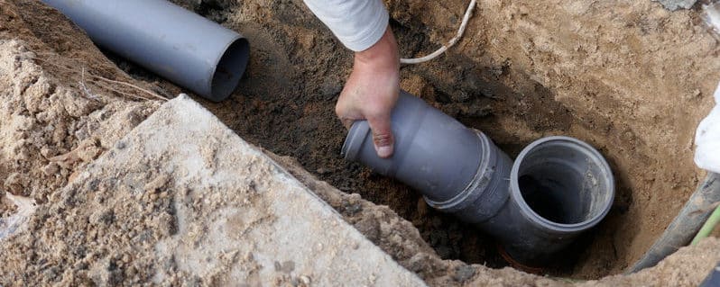 a hand reaching out to grab a disconnected pipeline in the ground
