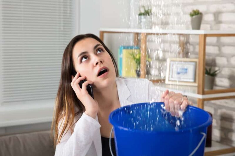 woman on the phone using a bucket to catch water falling from above