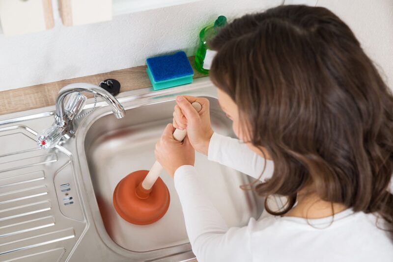 a woman using a plunger on her kitchen sink