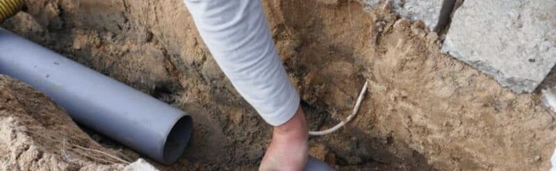 a hand reaching out to grab a disconnected pipeline in the ground