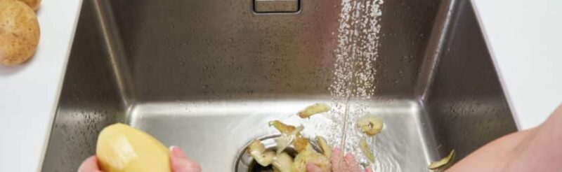 a woman pushing potato skins into the garbage disposal of her kitchen sink